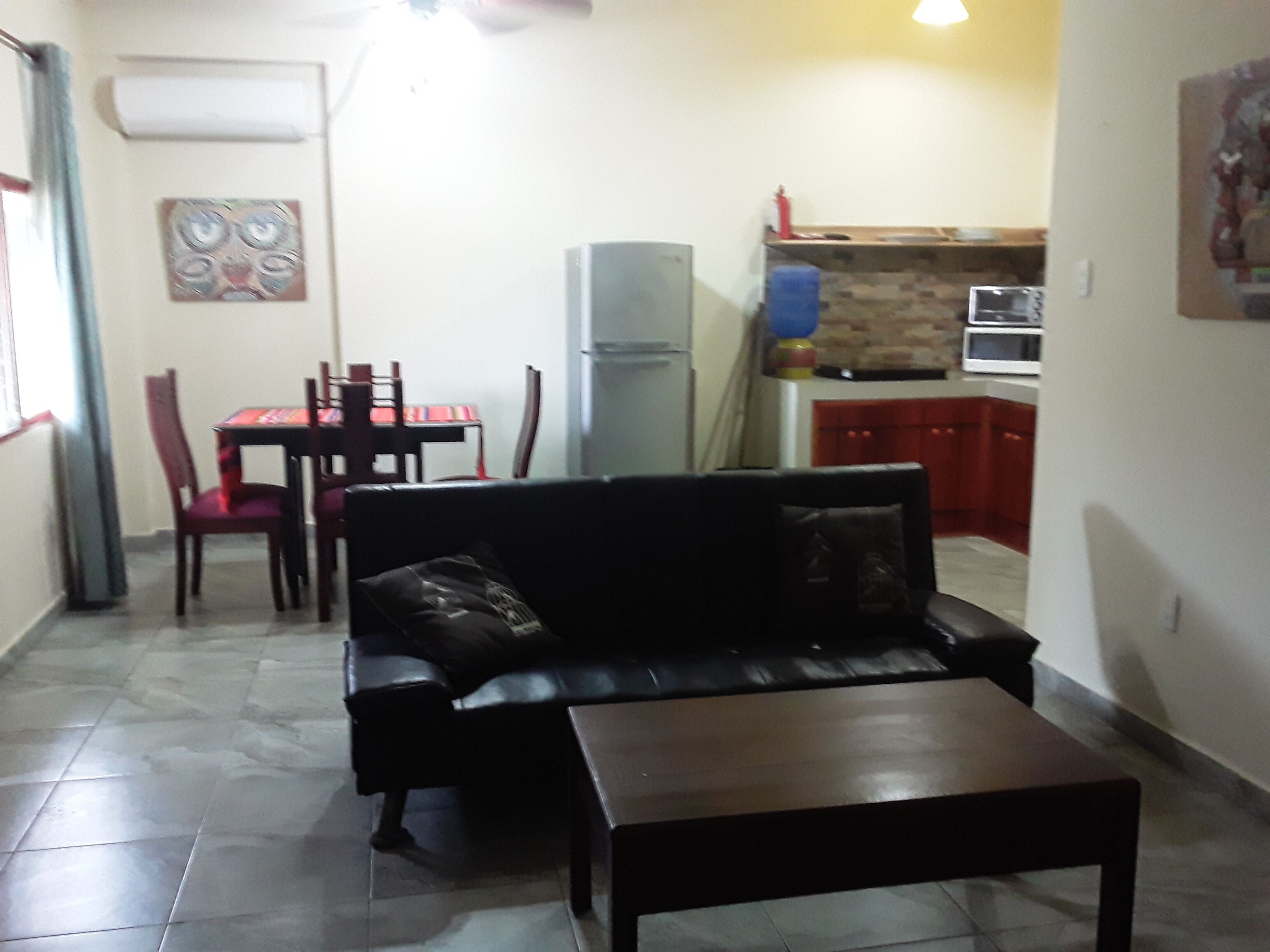 A living room with a black leather sofa, a wooden coffee table, and a dining area with a red table and chairs.