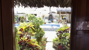 Una puerta de madera abierta que da a un patio con plantas en macetas y un área de piscina.