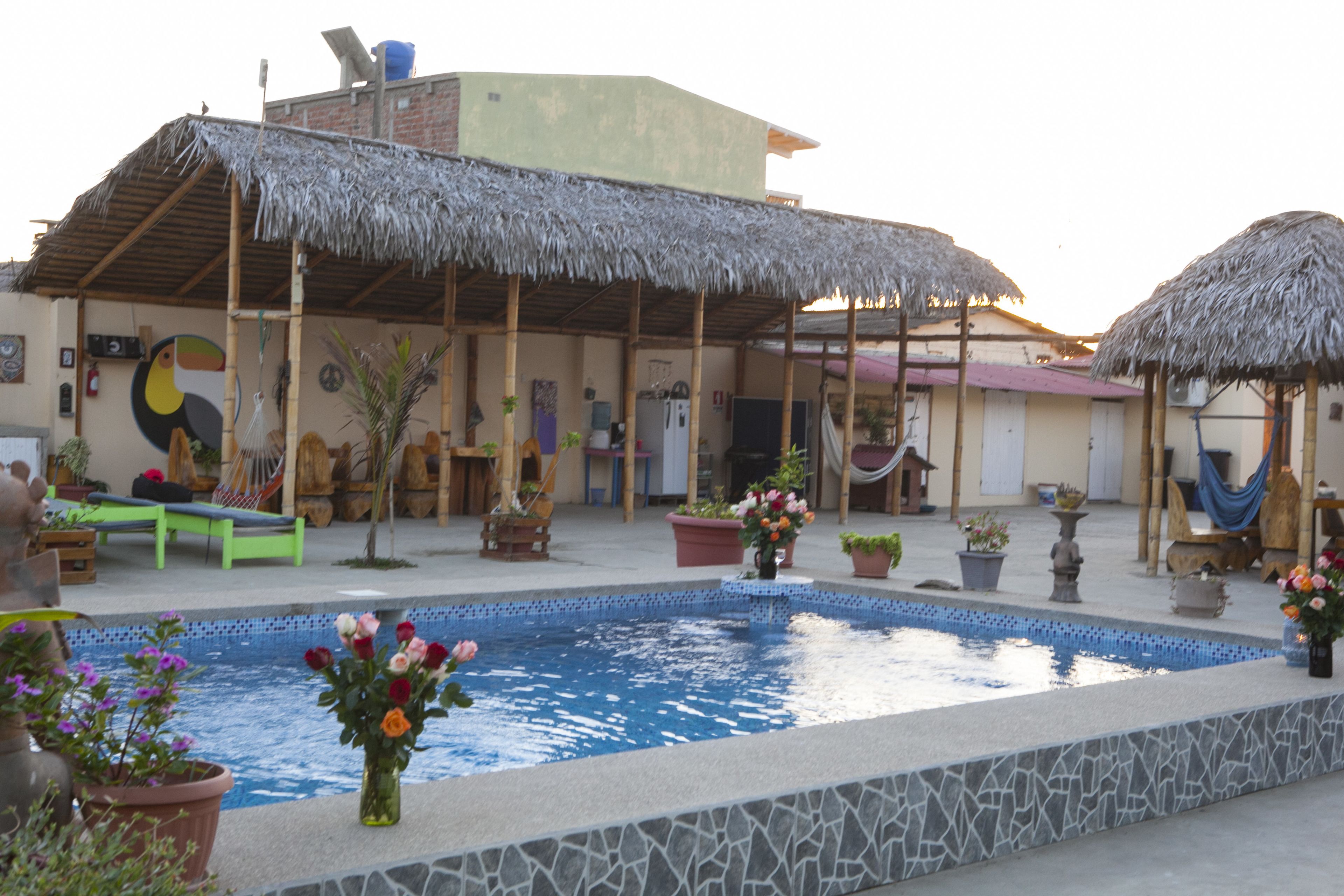 A pool area with a thatched-roof structure, a lounge chair, and potted plants.