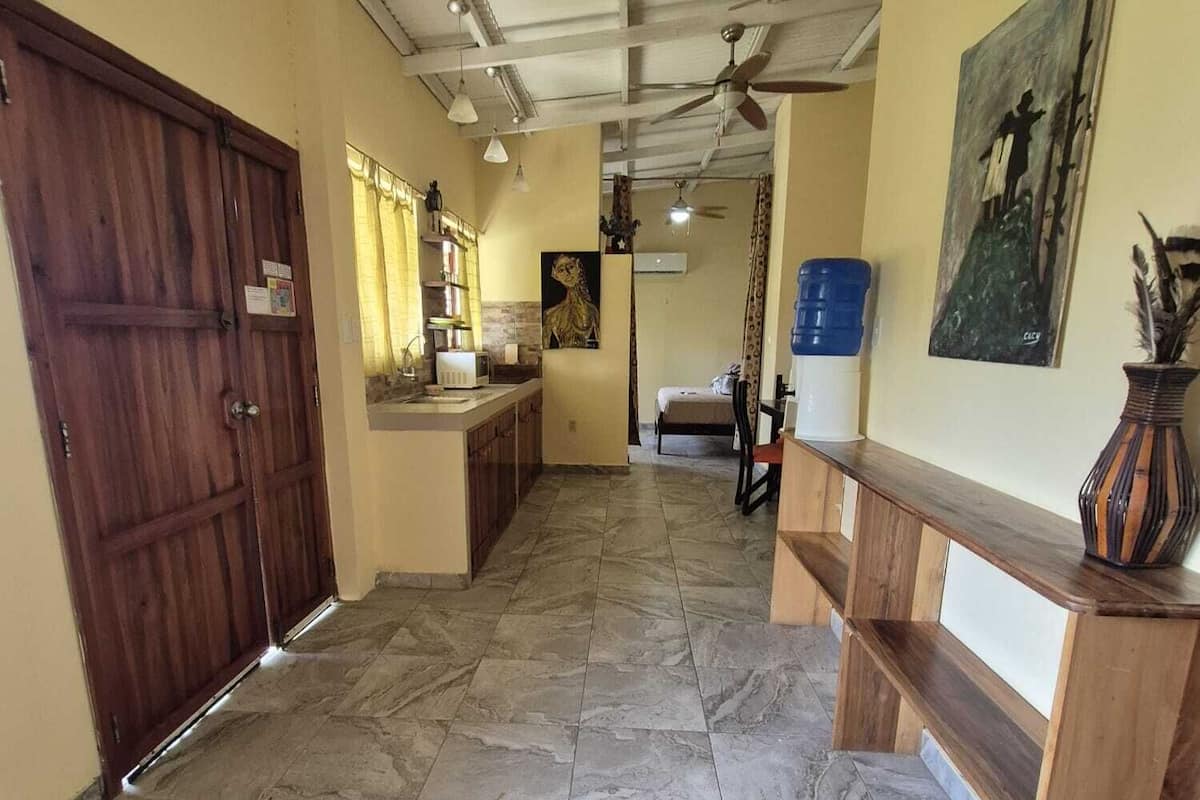 Un hall spacieux avec un sol en marbre, une porte en bois, un coin cuisine équipé d’un évier et de placards, et un ventilateur de plafond.