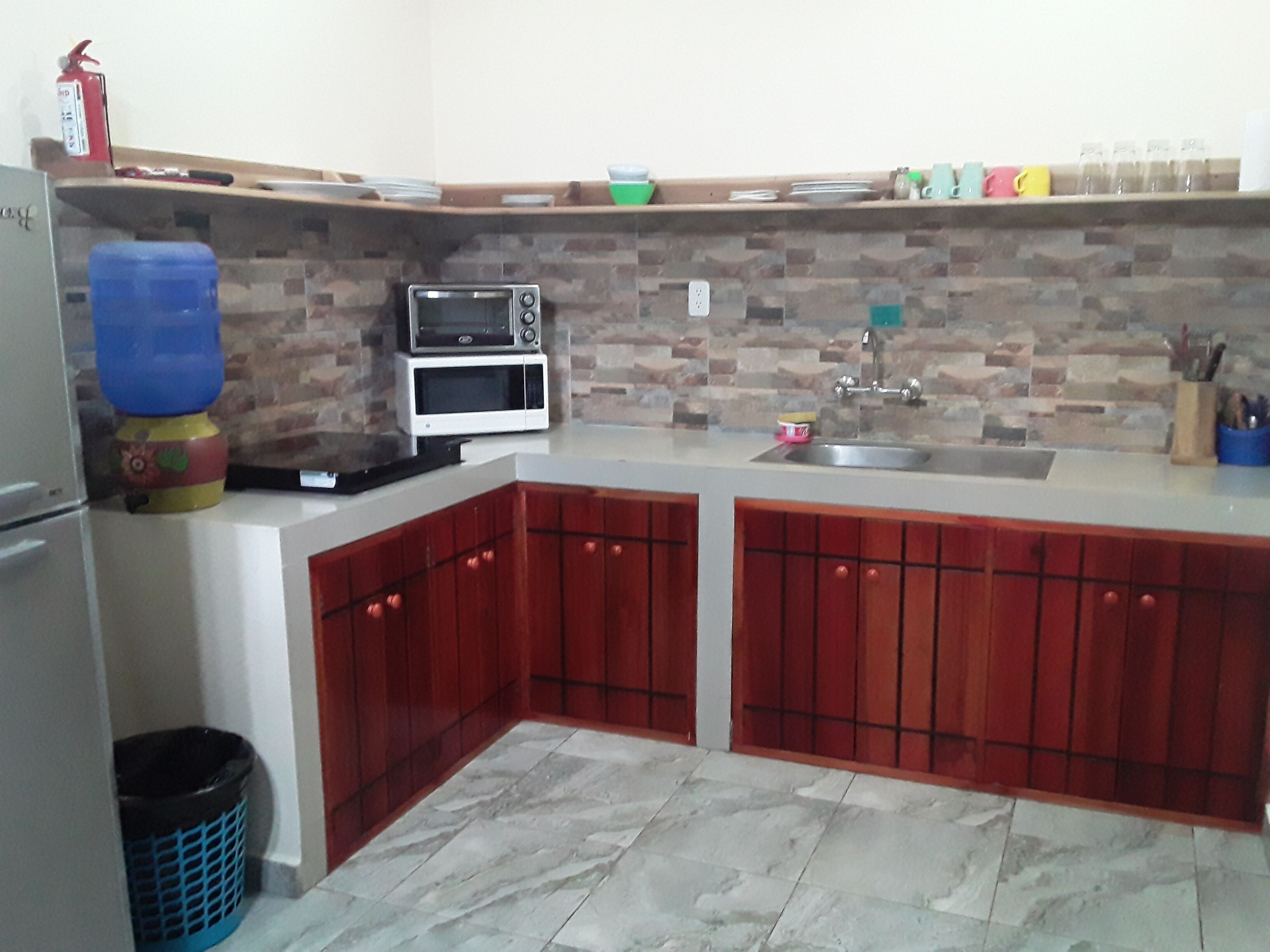 A compact kitchen with a microwave, sink, and red cabinets.