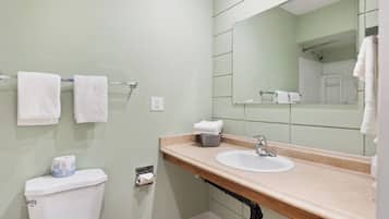 Un bagno con servizi igienici, lavabo e specchio. Asciugamani su uno stendino, un cesto e una confezione di carta igienica sul ripiano.
