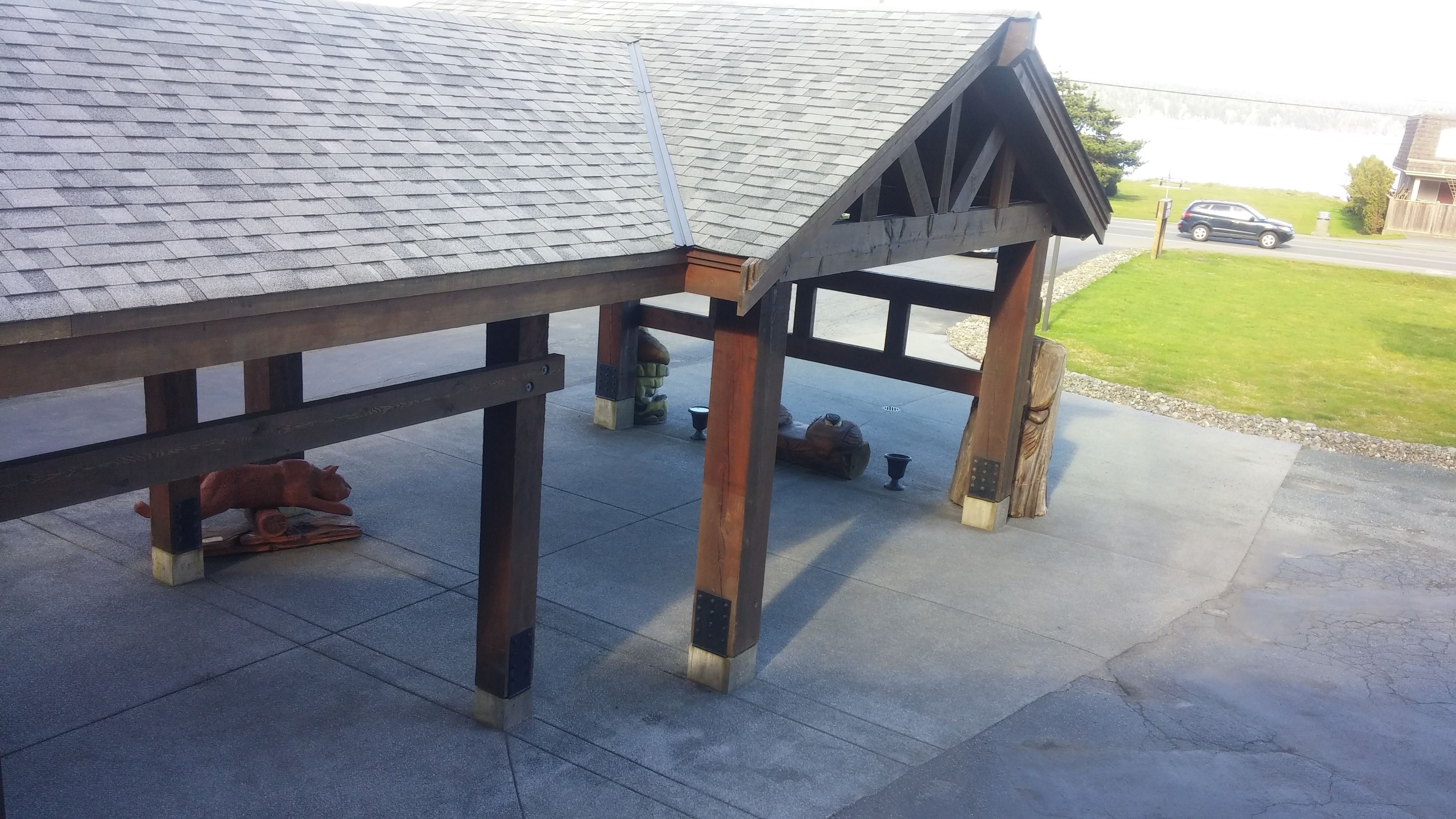A wooden gazebo with a sloped roof, supported by four pillars and a bench underneath.