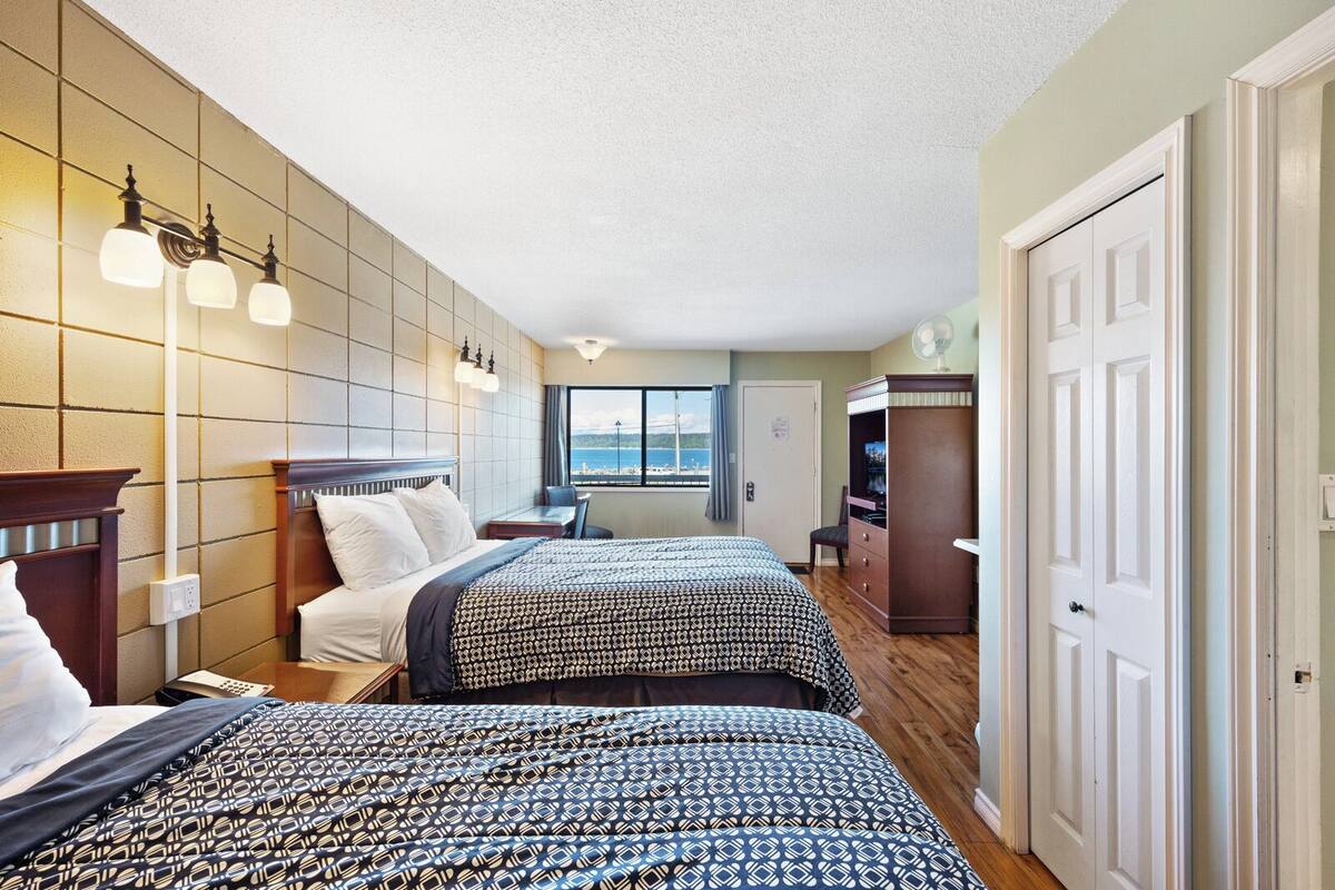 A hotel room with two beds, a desk, a TV, and a view of the sea.
