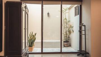 Quarto com porta de vidro deslizante que dá para uma varanda com plantas em vasos e uma pequena luminária externa.