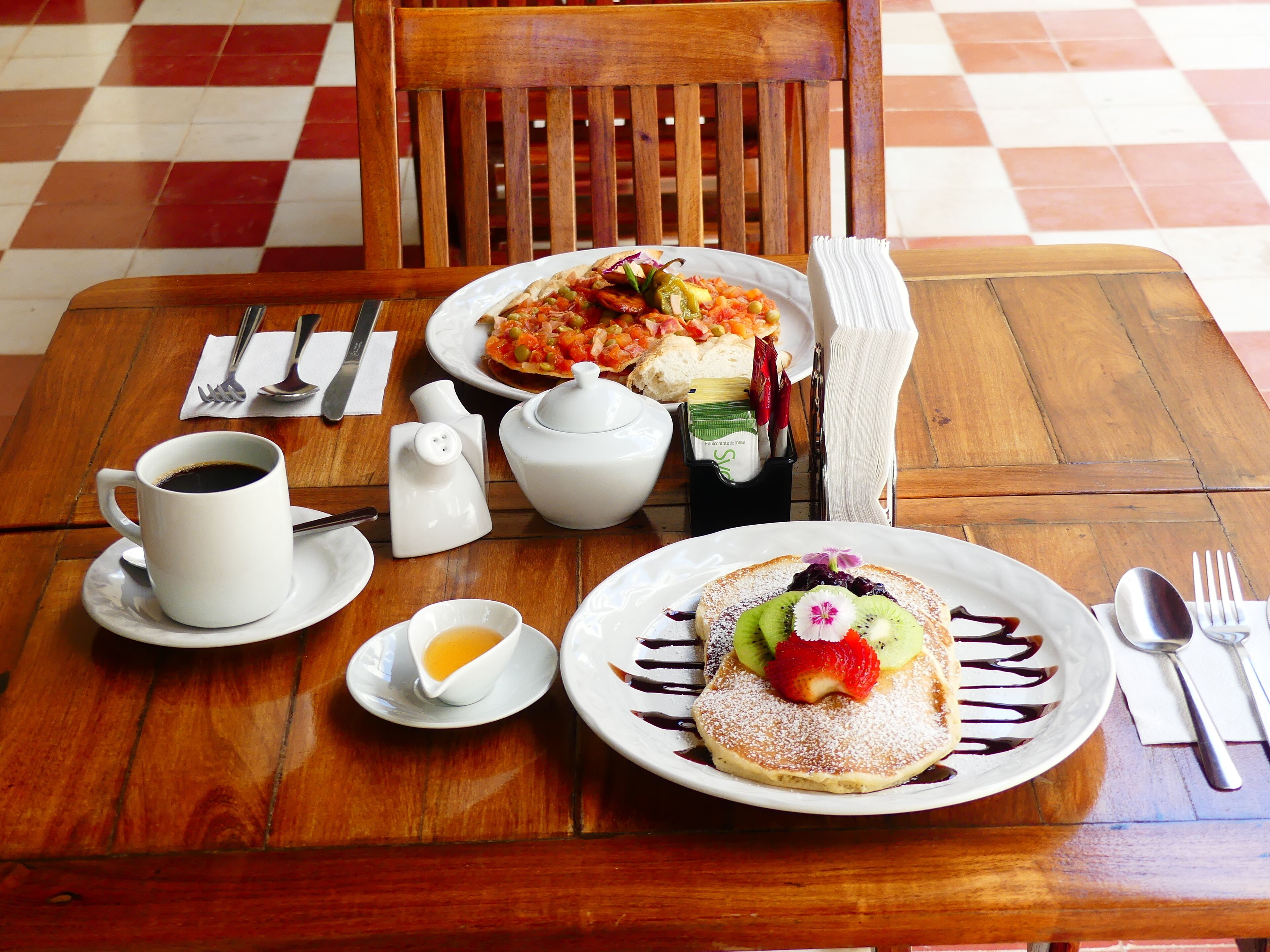 Une table en bois sur laquelle sont disposés des aliments pour le petit-déjeuner, notamment des crêpes, du café et une assiette de nourriture.
