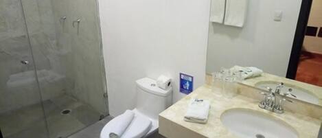 Un baño con cabina de ducha de vidrio, inodoro y lavamanos con espejo.
