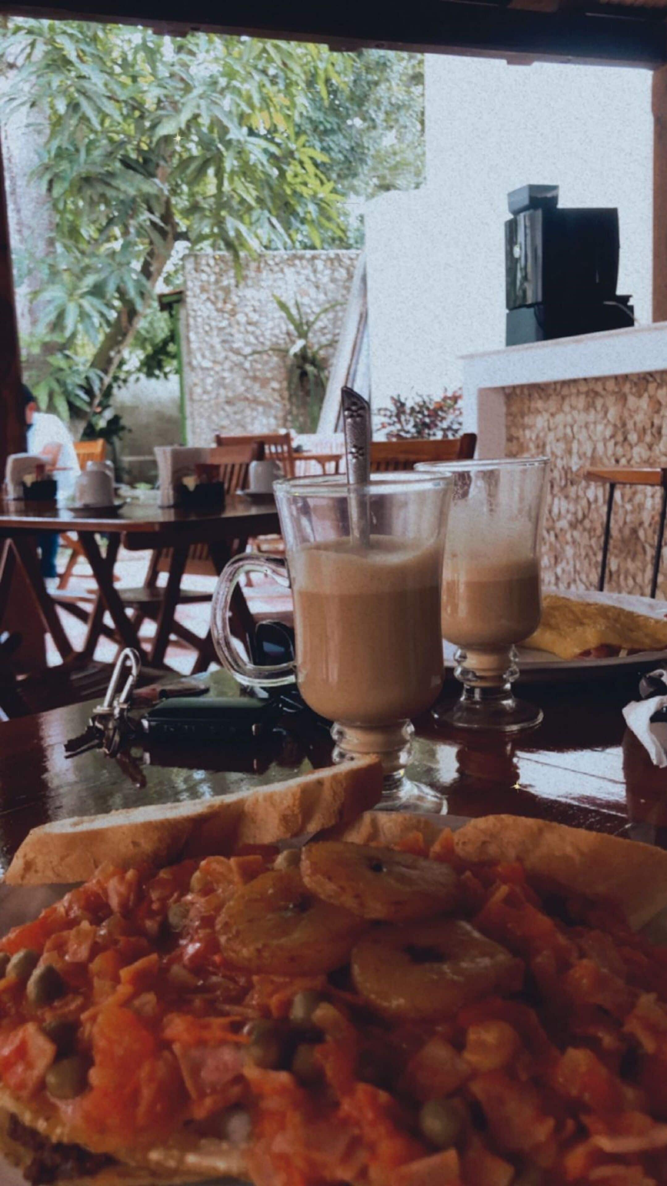 A dining table with a pizza, two glasses of a brown beverage, and a coffee machine.