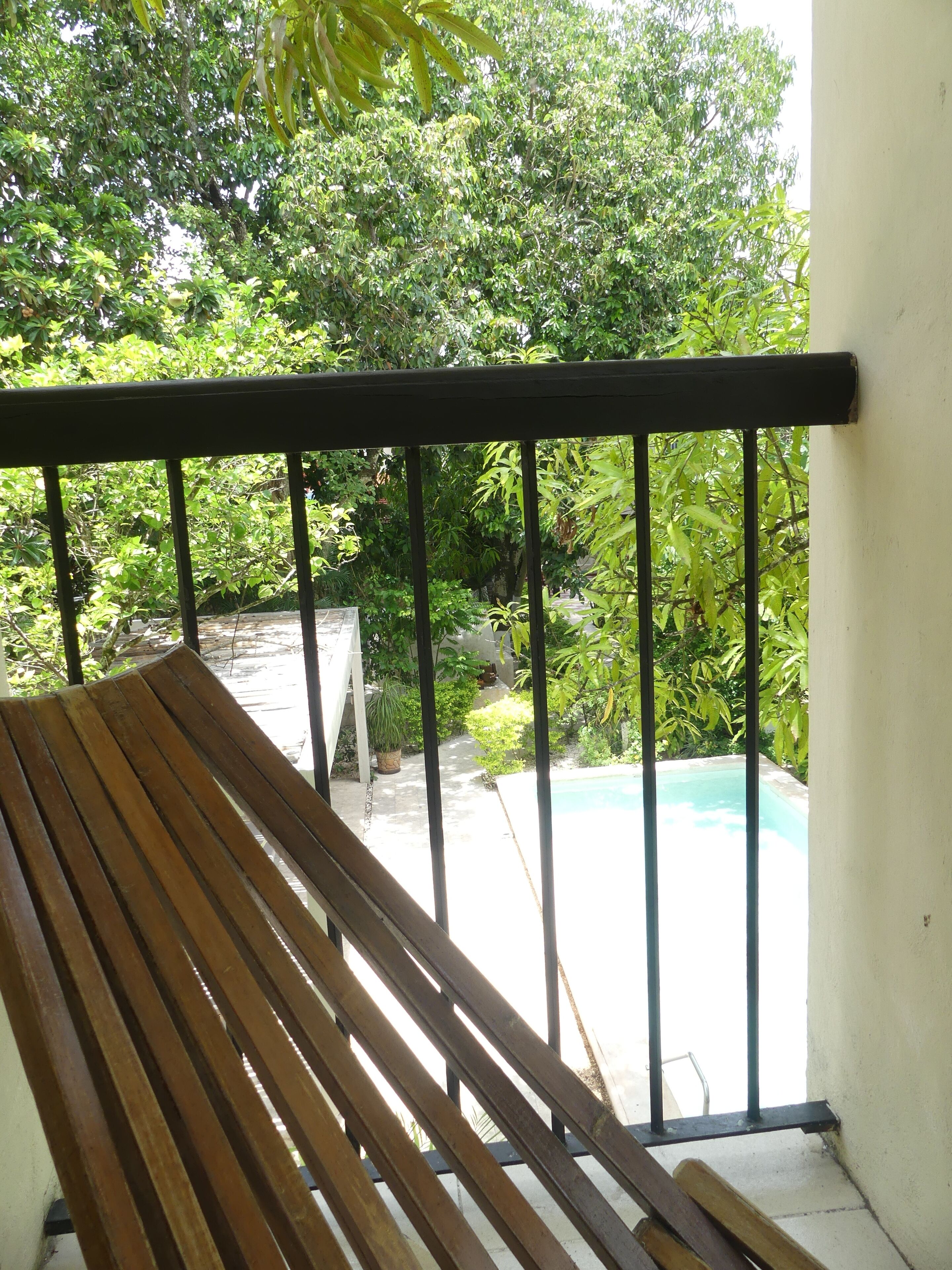A wooden bench with a metal railing, overlooking a swimming pool and lush greenery.