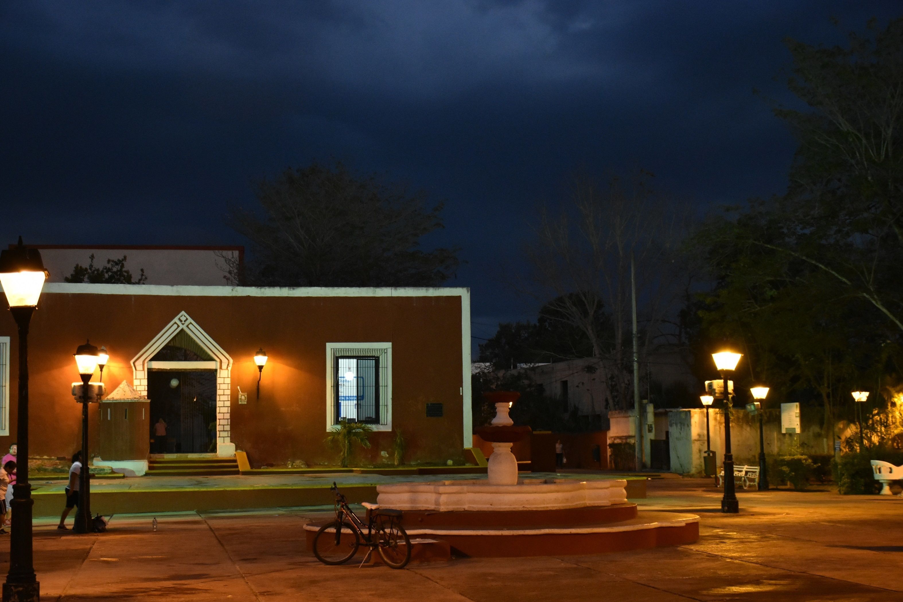A building with a prominent entrance, a fountain, and street lamps.