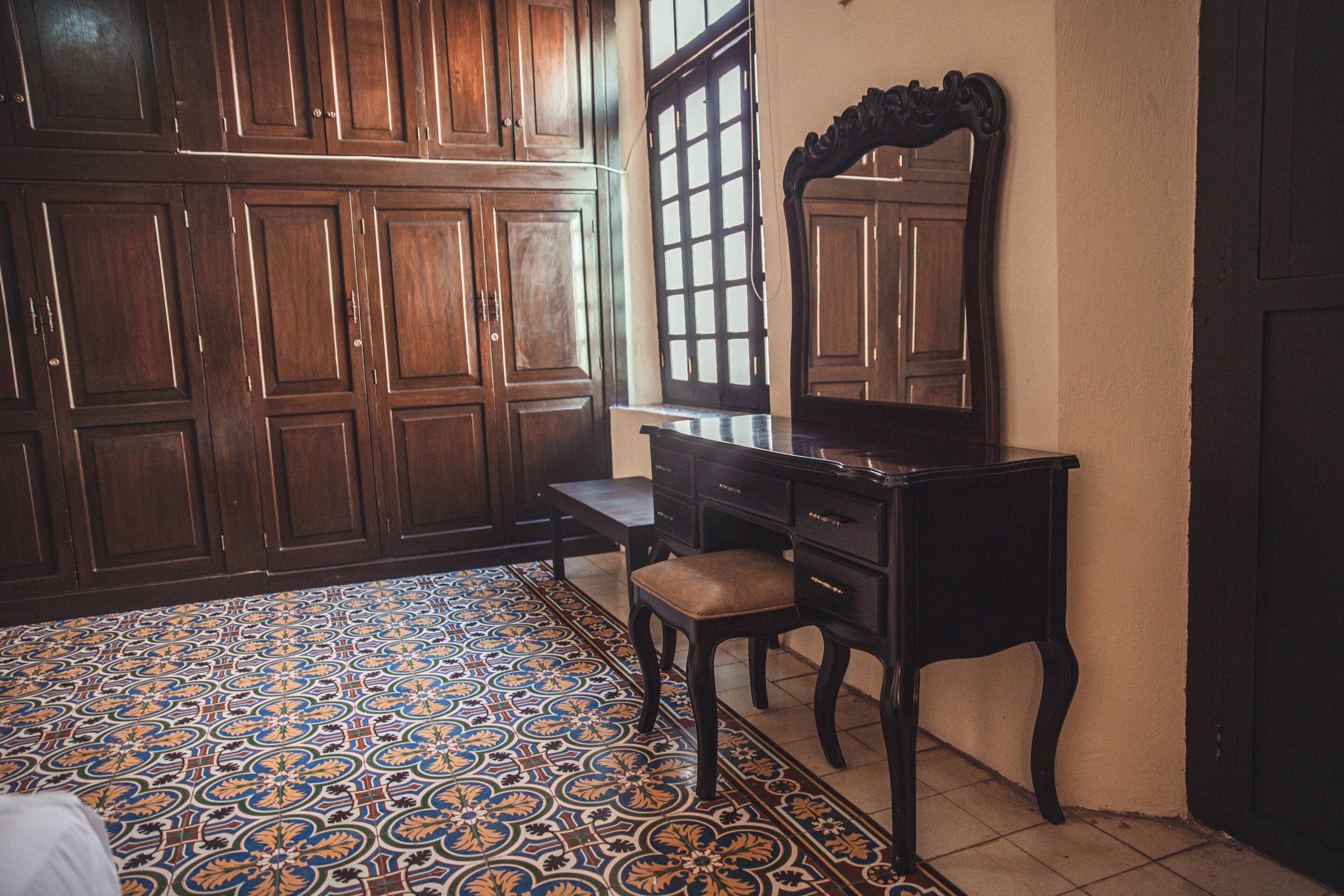 Une pièce avec une grande armoire en bois, un bureau doté d’un miroir et un sol à motifs.