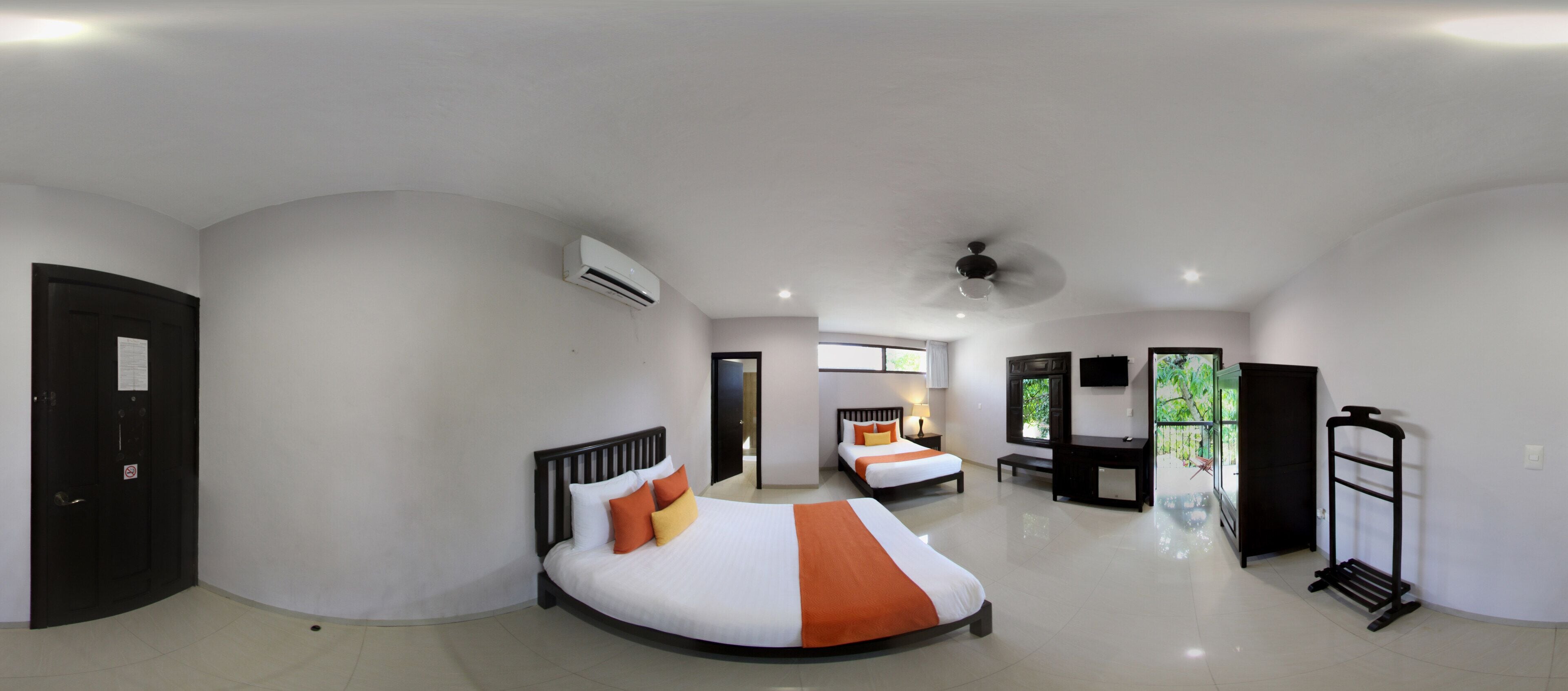 A hotel room with two beds, a ceiling fan, an air conditioning unit, a TV, and a balcony with a view of greenery.
