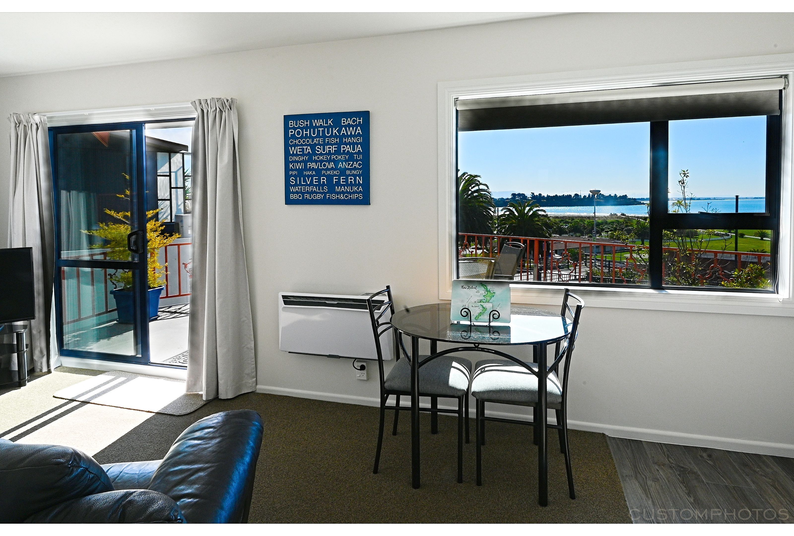 Et værelse med spisebord, stole, sofa, stort vindue med havudsigt og et skilt, der viser faciliteter.