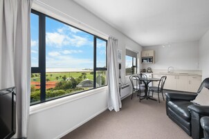 A modern room with a large window, a dining area, and a kitchen.