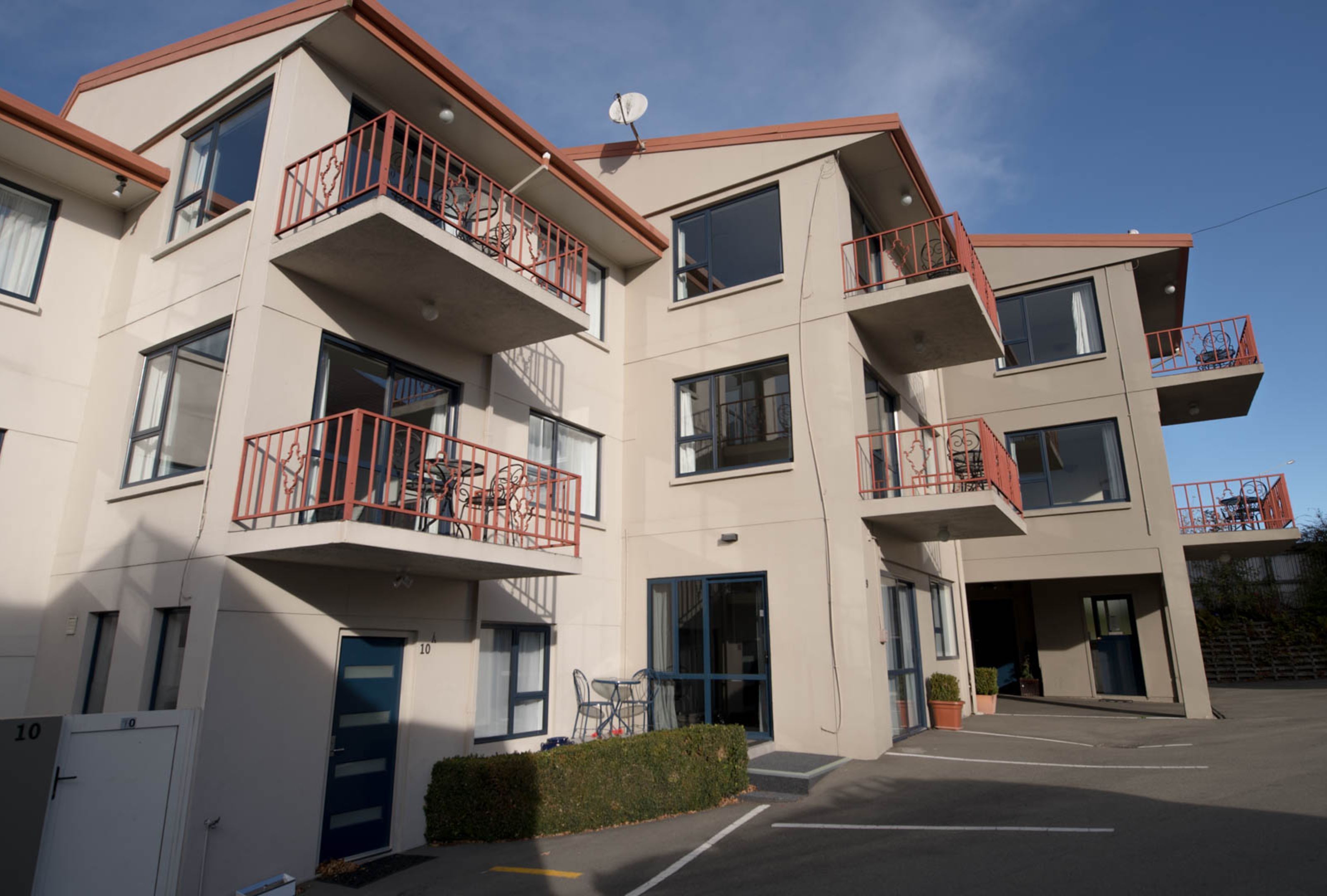 A multi-story building with balconies, large windows, and a parking area.