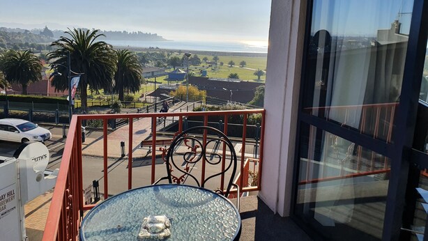 Un balcón con una mesa y sillas de vidrio, con vista a una zona costera con palmeras y una vista despejada del mar.