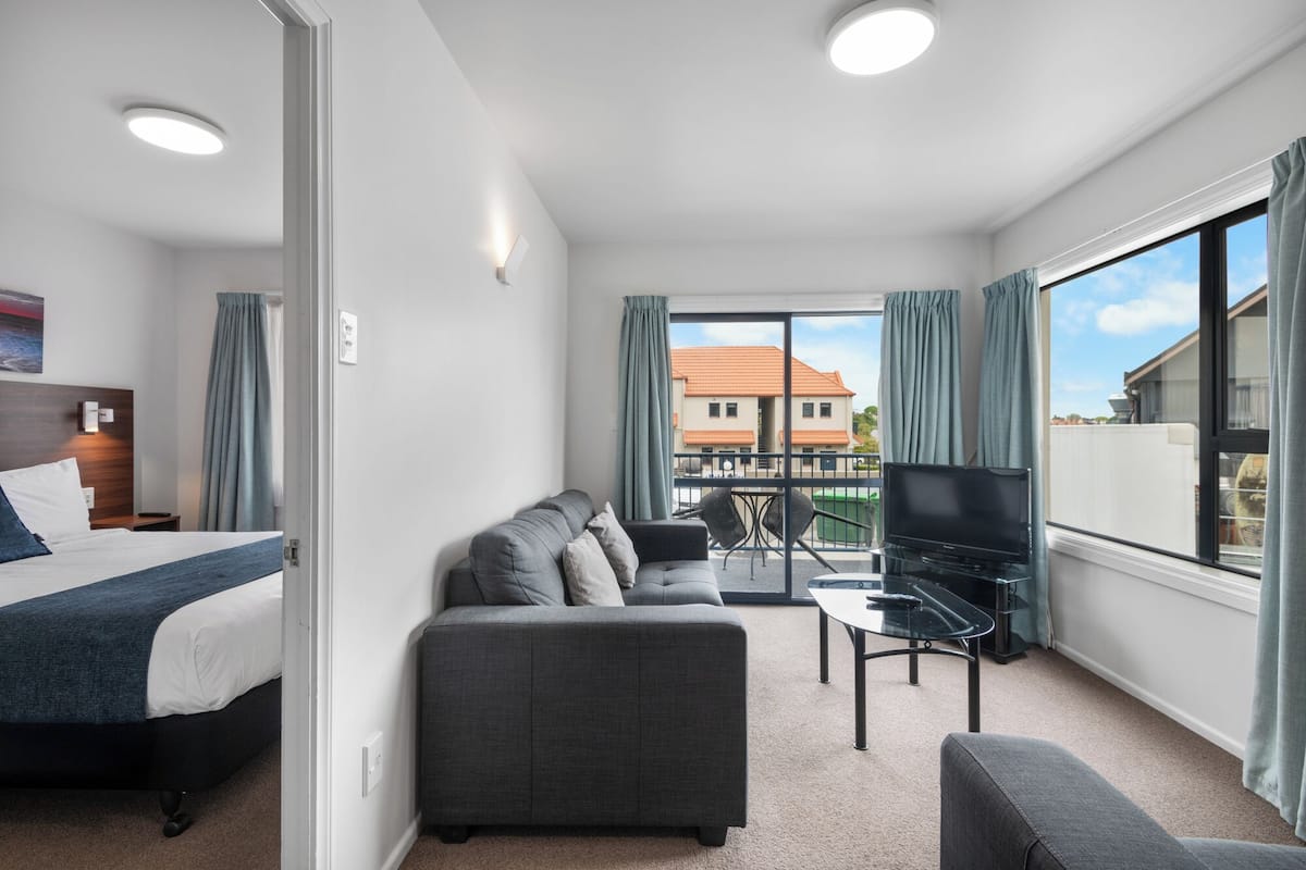 Ein Hotelzimmer mit Bett, Sofa, Fernseher und einem Balkon mit Blick auf Gebäude.
