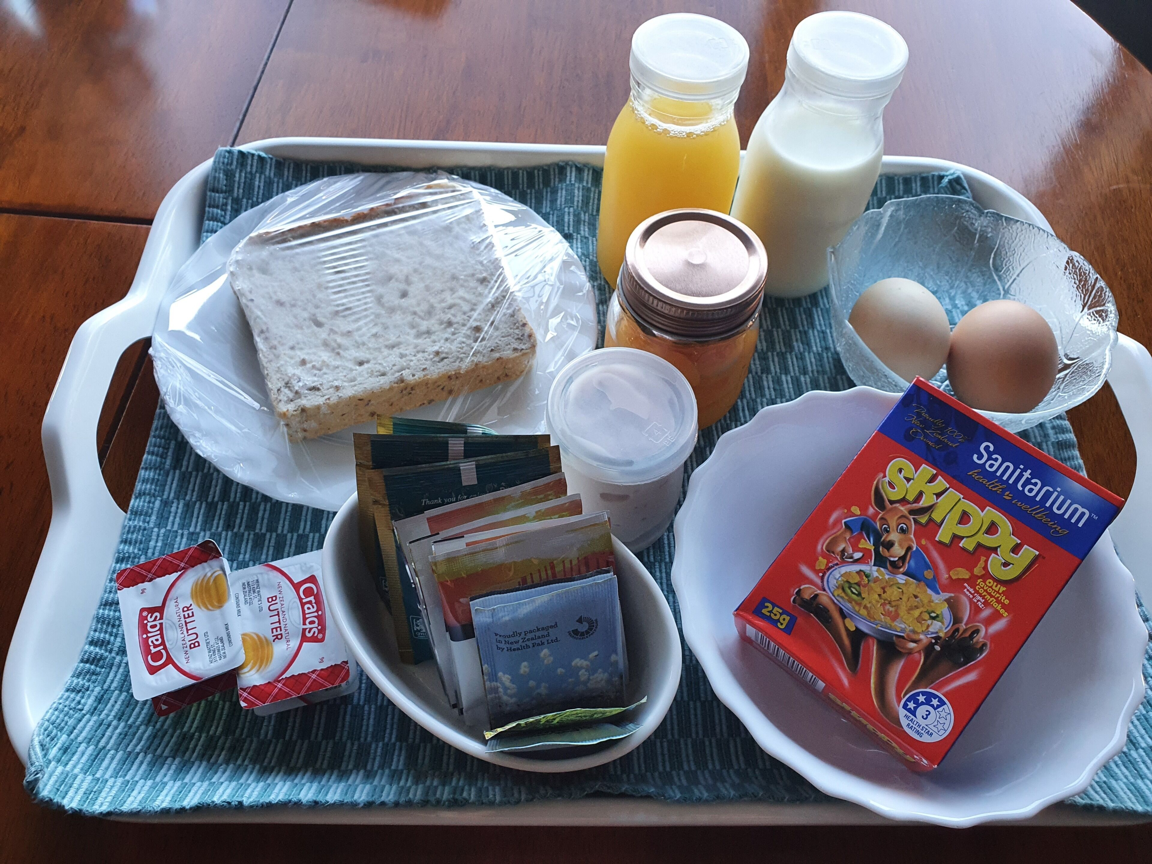 A tray with bread, butter, milk, eggs, cereal, and juice.