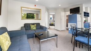 Una sala moderna con un sofá gris, una mesa de centro y un televisor. Hay un comedor con una mesa y sillas.