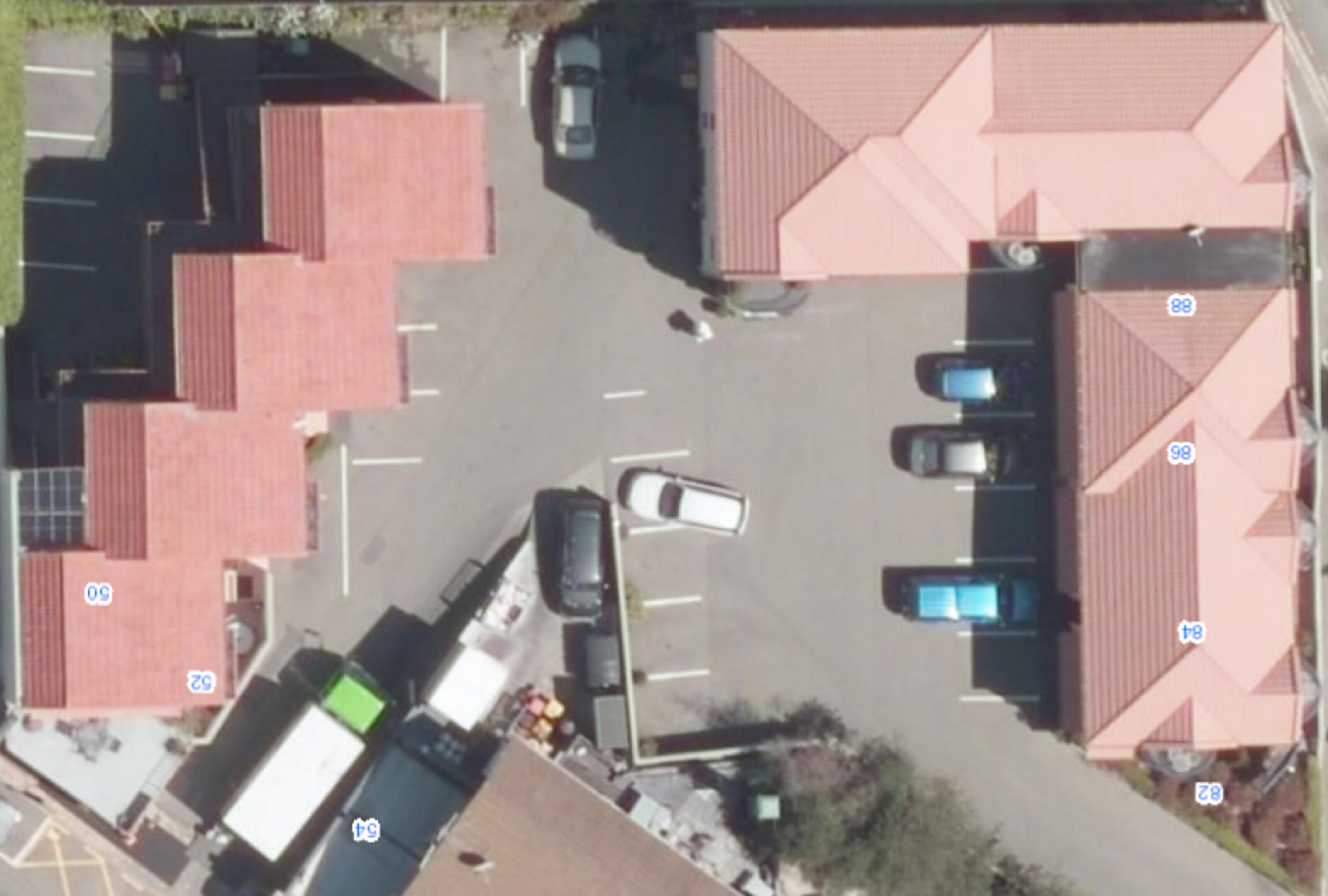 Ein Luftbild eines Parkplatzes mit mehreren Autos, einem weißen Lastwagen und einem Gebäude mit roten Ziegeldächern.