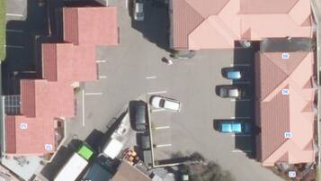 An aerial view of a parking lot with several cars, a white truck, and a building with red-tiled roofs.