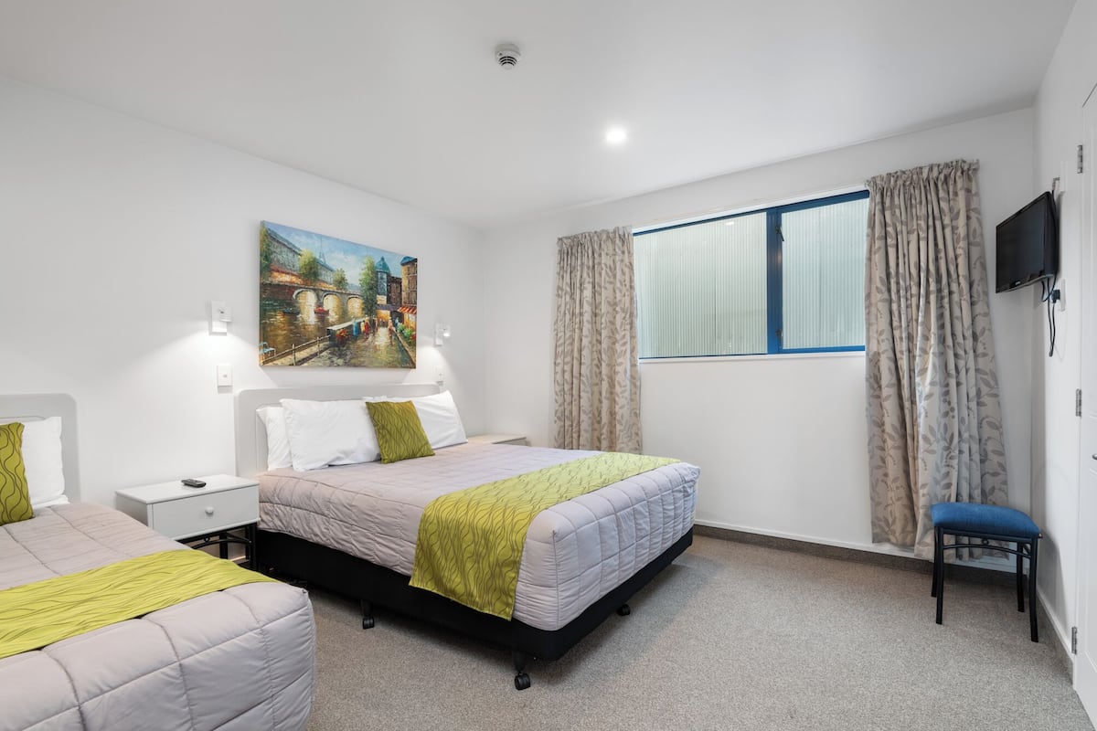Ein Hotelzimmer mit Bett, Stuhl, Schreibtisch, einem Gemälde und einem fenster mit Vorhängen.