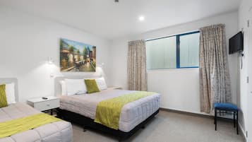 A hotel room with a bed, a chair, a desk, a painting, and a window with curtains.