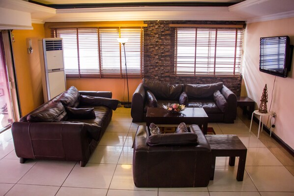 A living room with two leather sofas, a coffee table, and a TV mounted on the wall. - EED Pension Boutique Hotel (Lagos)