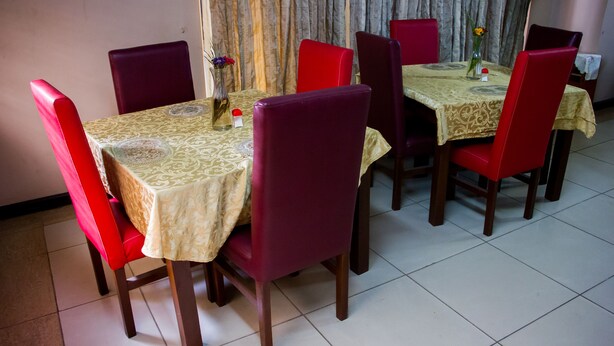 A dining area with a table set for four, surrounded by red chairs, and a vase with flowers on the table. - EED Pension Boutique Hotel (Lagos)