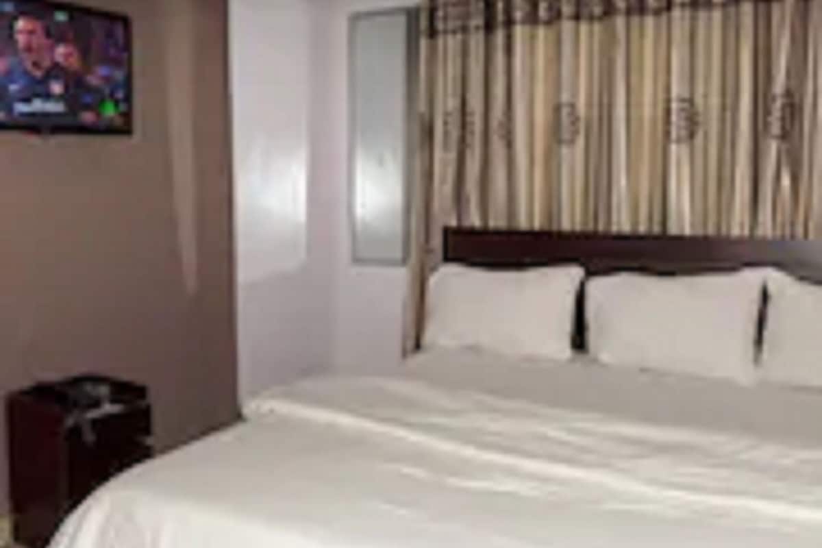A hotel room with a large bed, a television on the wall, and a curtain with a pattern.