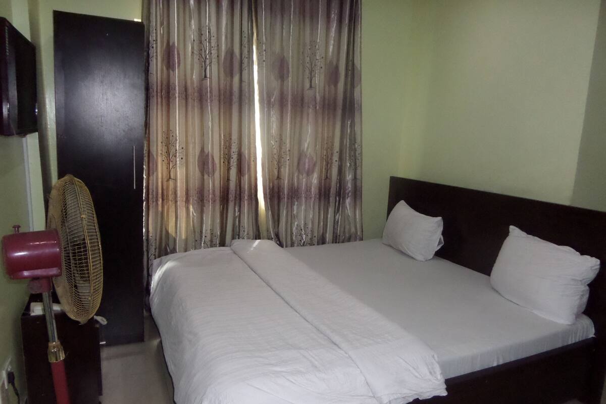A room with a bed, a fan, and a curtain.