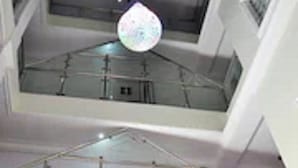 Un intérieur à plusieurs niveaux doté d’un atrium central, de rampes en verre et d’un luminaire décoratif en forme de sphère.