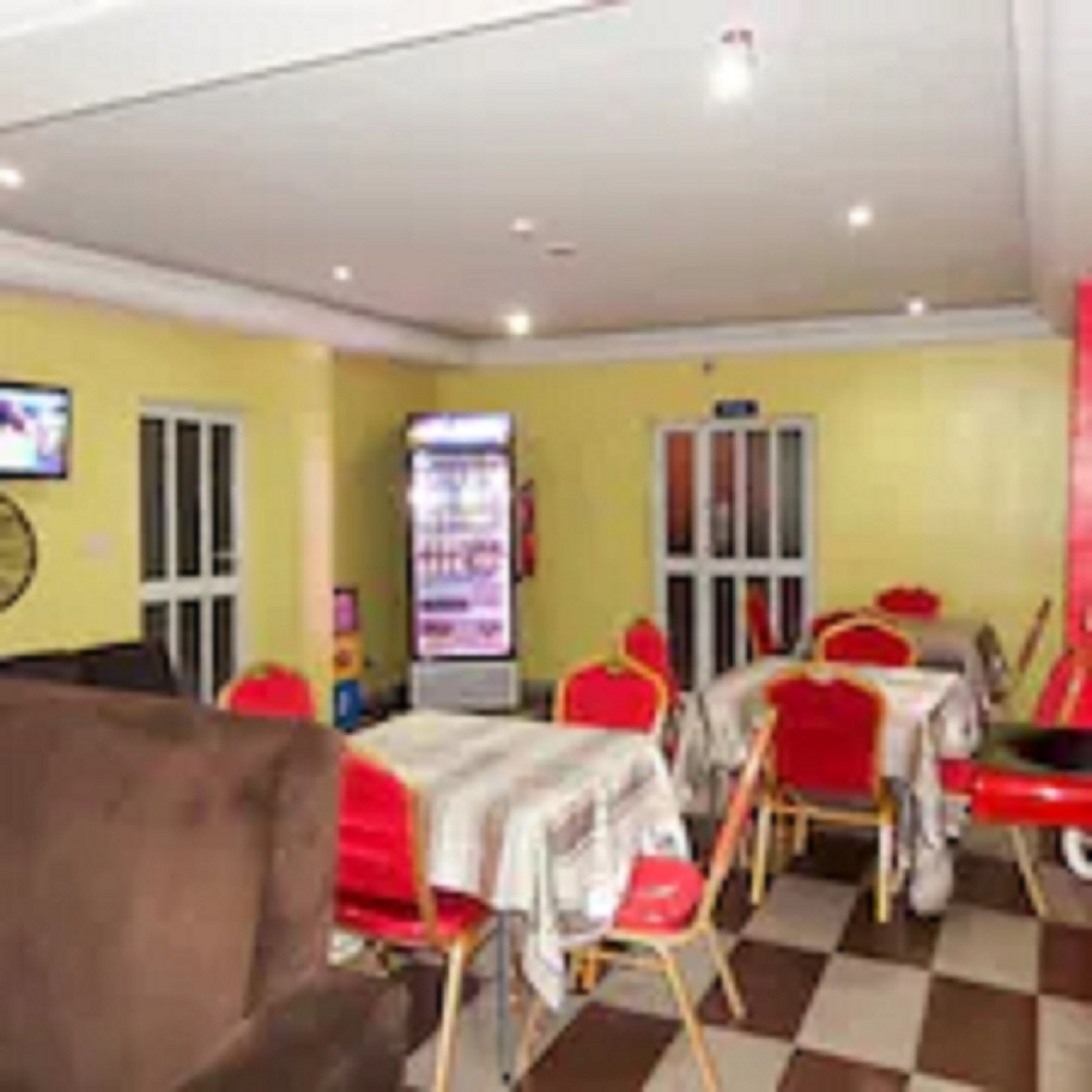 A restaurant interior with yellow walls, red chairs, and checkered flooring.