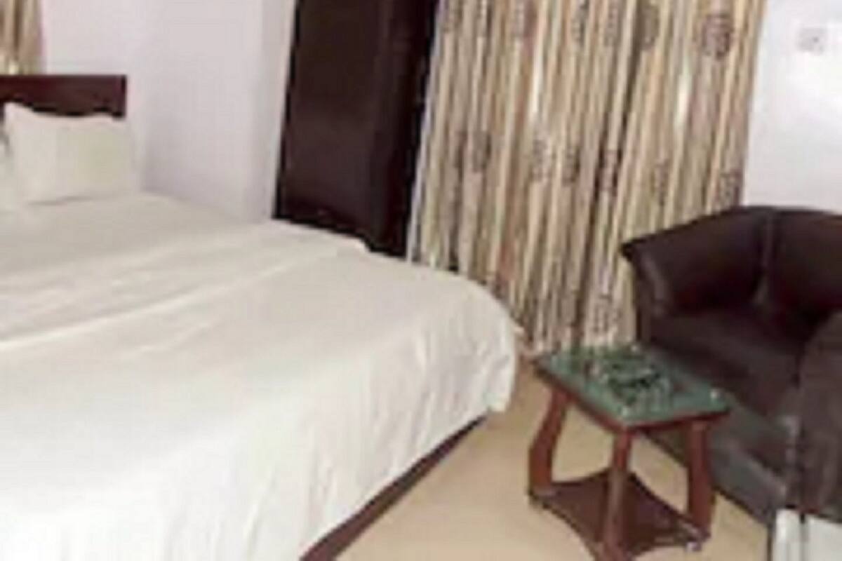 A bedroom with a bed, a dark-colored wardrobe, a small table, and a chair.