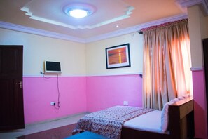 A bedroom with a bed, a television mounted on the wall, and a window with curtains. - Maria Suites (Lagos)
