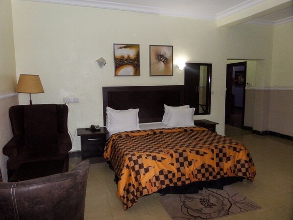 Habitación de hotel con cama, una silla, mesita de noche, lámpara y dos cuadros colgados en la pared.