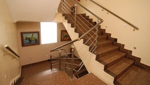 A staircase with a metal railing, a fire extinguisher on the wall, and a painting on the wall. - Trafford Hotel (Abuja)