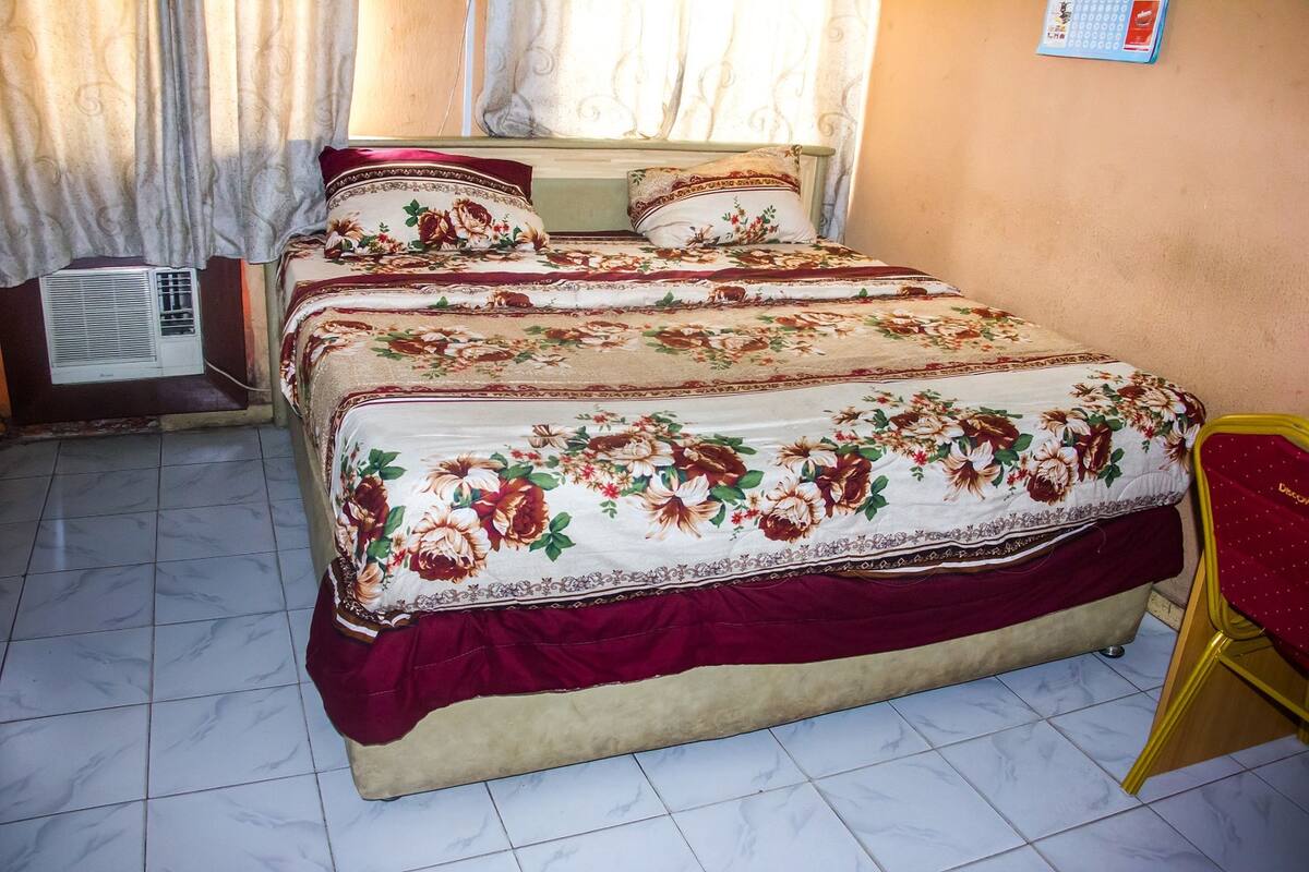 Ein Doppelbett mit floraler Bettwäsche, einem roten Zierkissen und einem gelben Sessel.