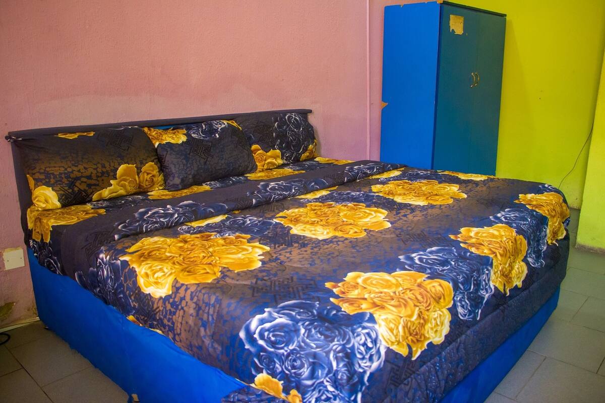 Ein Bett mit blumigem Überwurf, einem blauen Kopfteil und einem blauen Kleiderschrank vor einer rosafarbenen Wand.