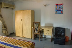 A room with a bed, a wooden wardrobe, a desk with a chair, and a black leather chair. - Oak Hotels (Lagos)