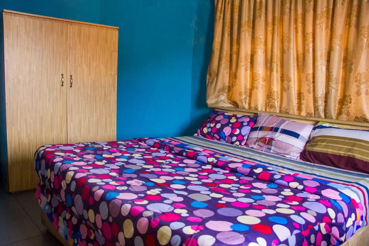 Ein Schlafzimmer mit einem Bett, das mit einer bettenwäsche mit Punkten bezogen ist, einem Holzschrank und einem Fenster mit blumigen Vorhängen.