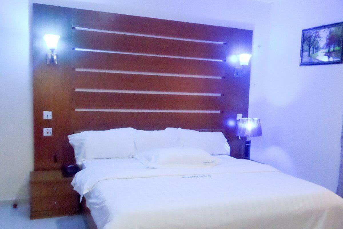 A hotel room with a wooden headboard, a bed with white bedding, two bedside lamps, and a framed picture on the wall.