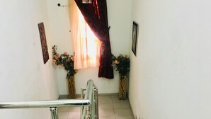 Una escalera con barandillas metálicas, una ventana con cortinas, y dos arreglos florales a cada lado.