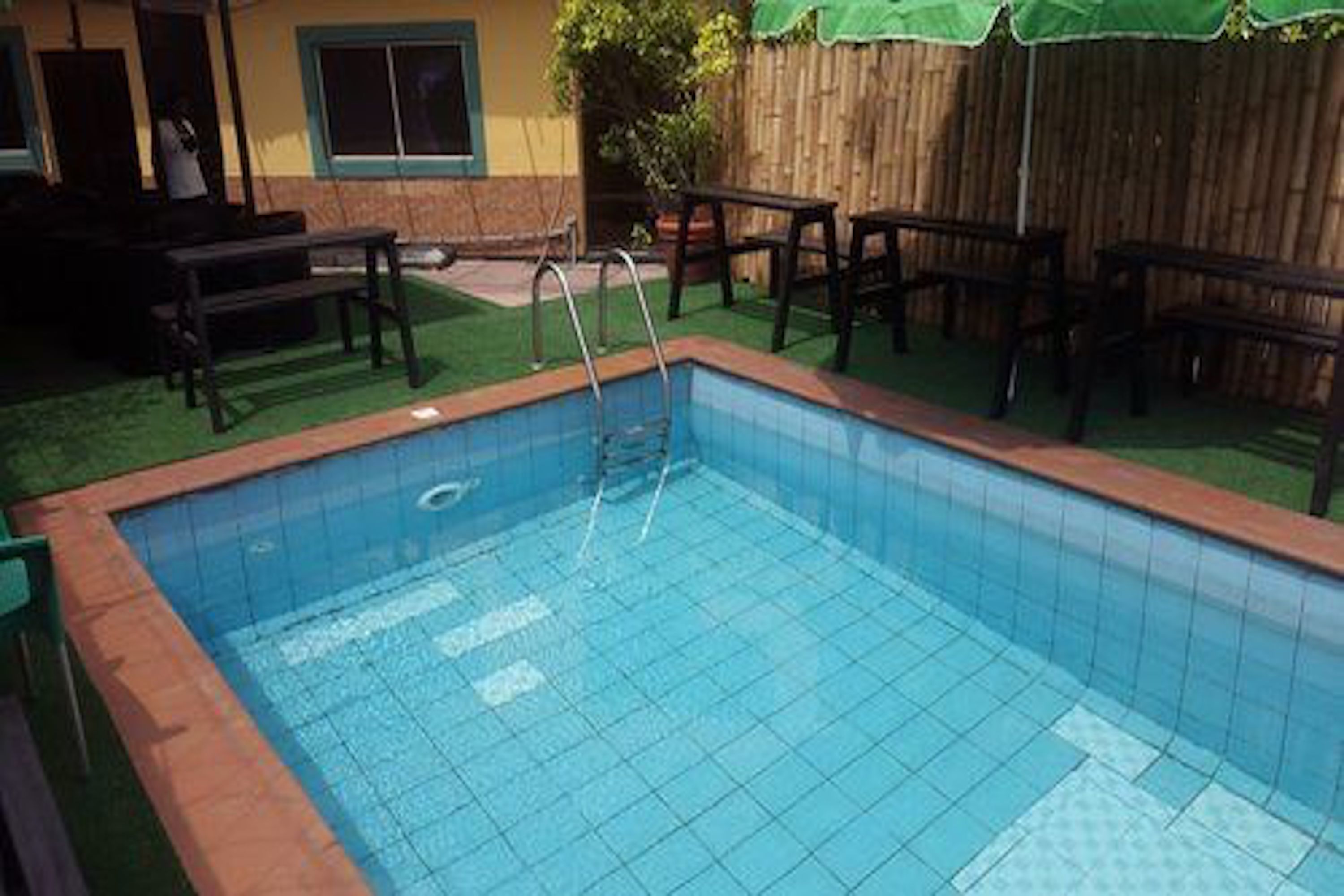 En rektangulär swimmingpool med en stege, omgiven av ett trästaket och en grön gräsmatta.