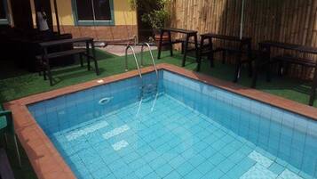 Une piscine rectangulaire avec un escalier, entourée d’une clôture en bois et d’une pelouse verdoyante.