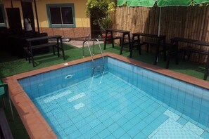 A rectangular swimming pool with a ladder, surrounded by a wooden fence and a green lawn.