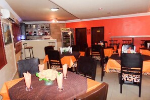 A restaurant with tables set for dining, a bar area with bottles, and a counter.