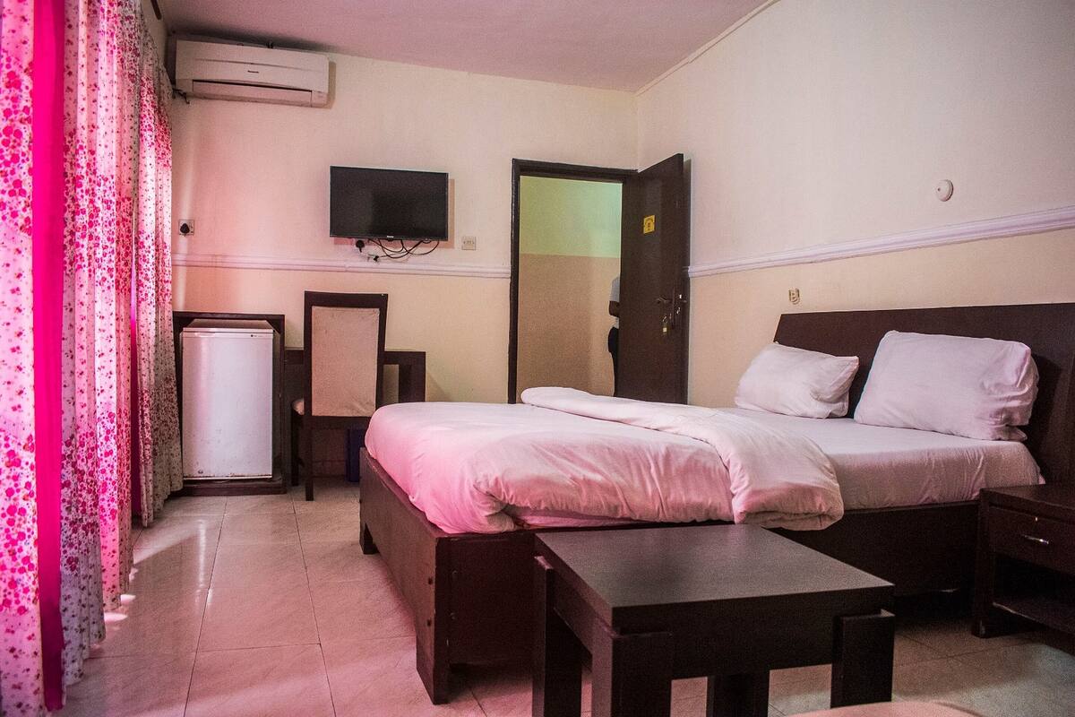 A hotel room with a bed, bedside table, a small desk, a television mounted on the wall, and a door.