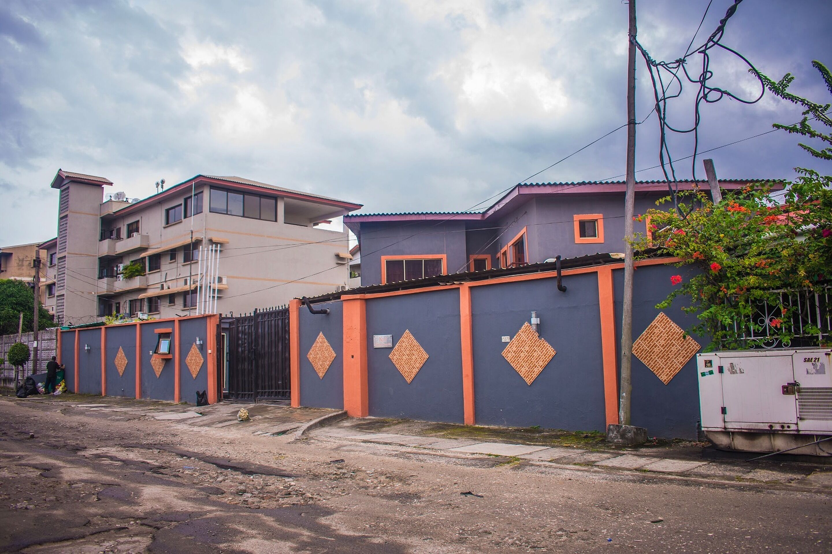 A residential area with a gated compound, a utility box, and a building with a tiled roof.