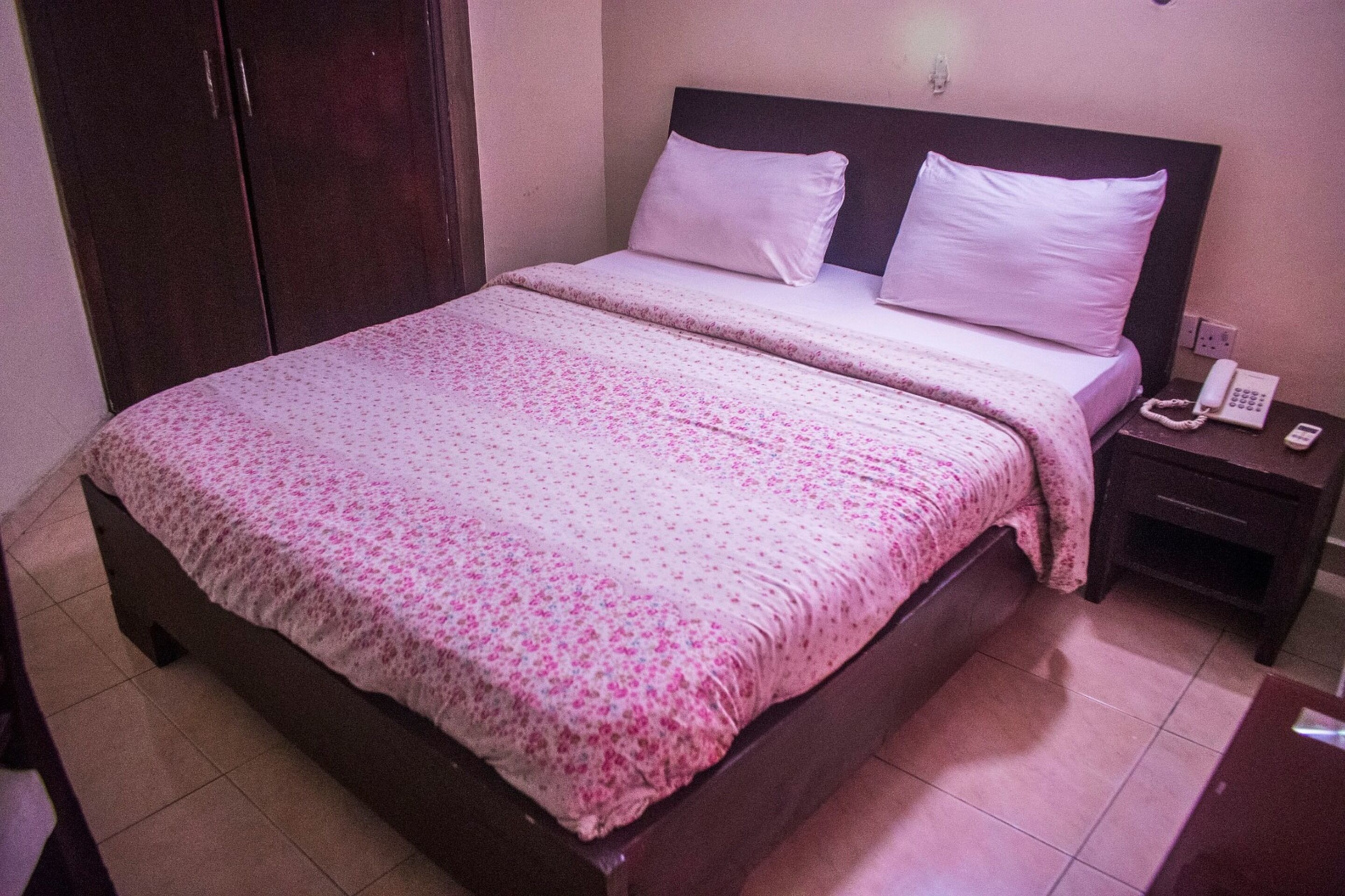 A standard hotel room with a bed, a nightstand, a telephone, and a wardrobe.